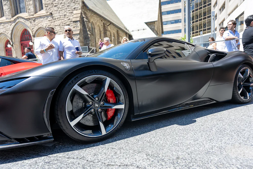 Matte-black sports car at a curbside car show with onlookers.