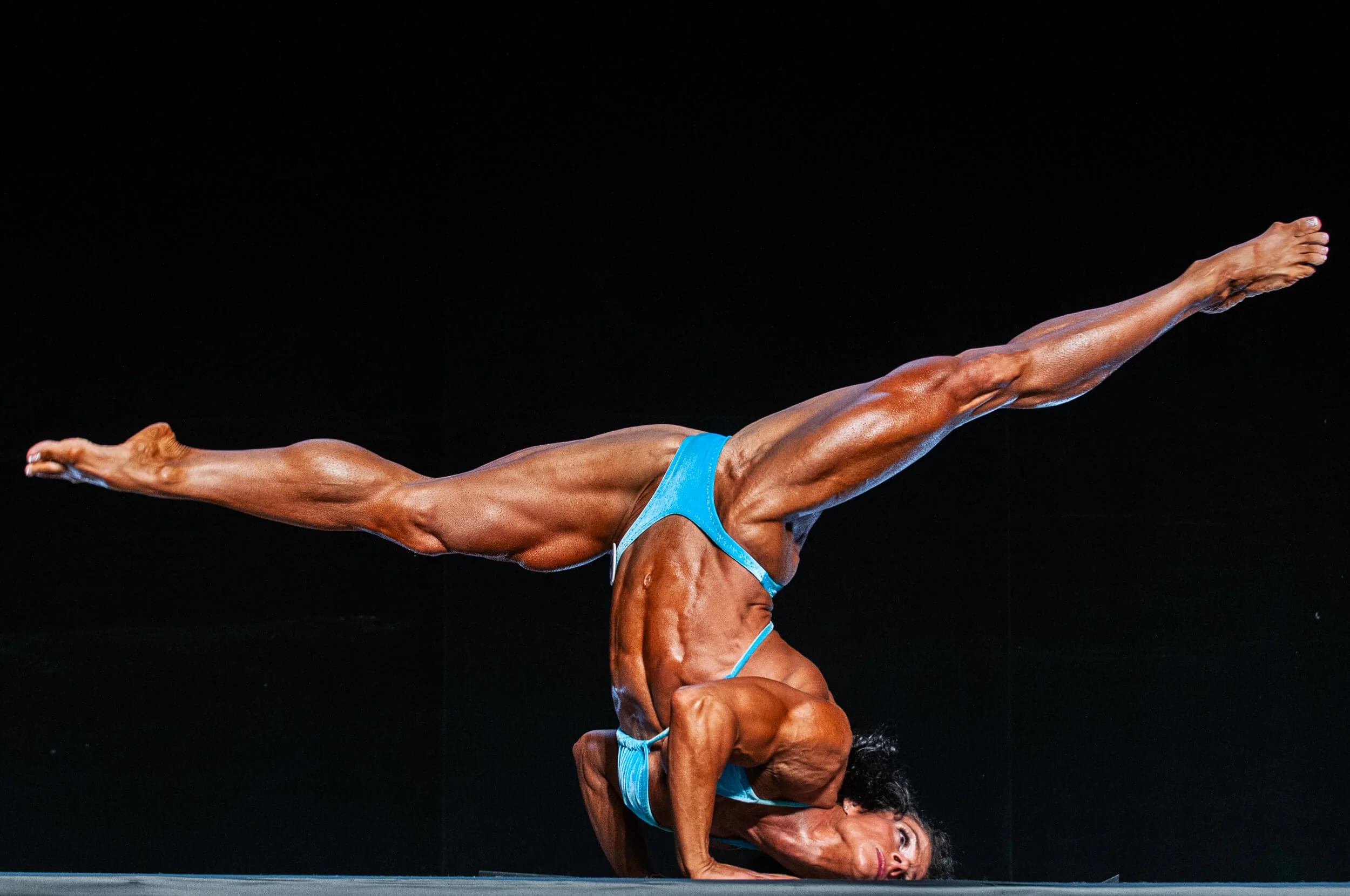 Fitness performer in an inverted stage pose, showing a frame where body position and full-shape composition matter more than a centered face.