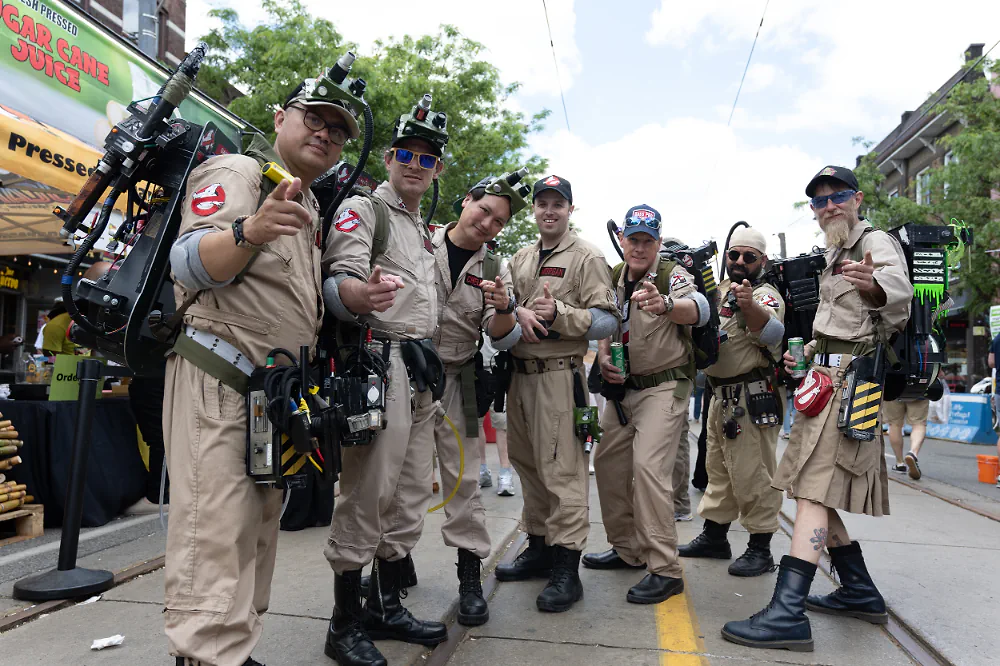 Group of Ghostbusters cosplayers posing on a closed street at a community festival.