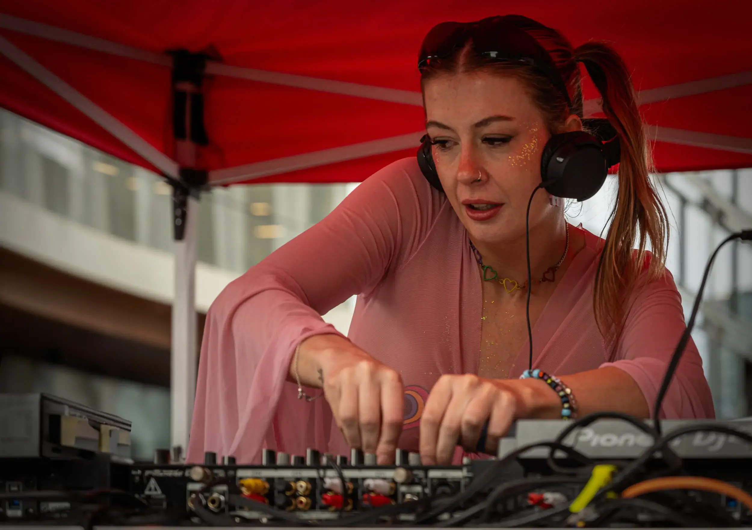 DJ working headphones and mixer under a red event tent.